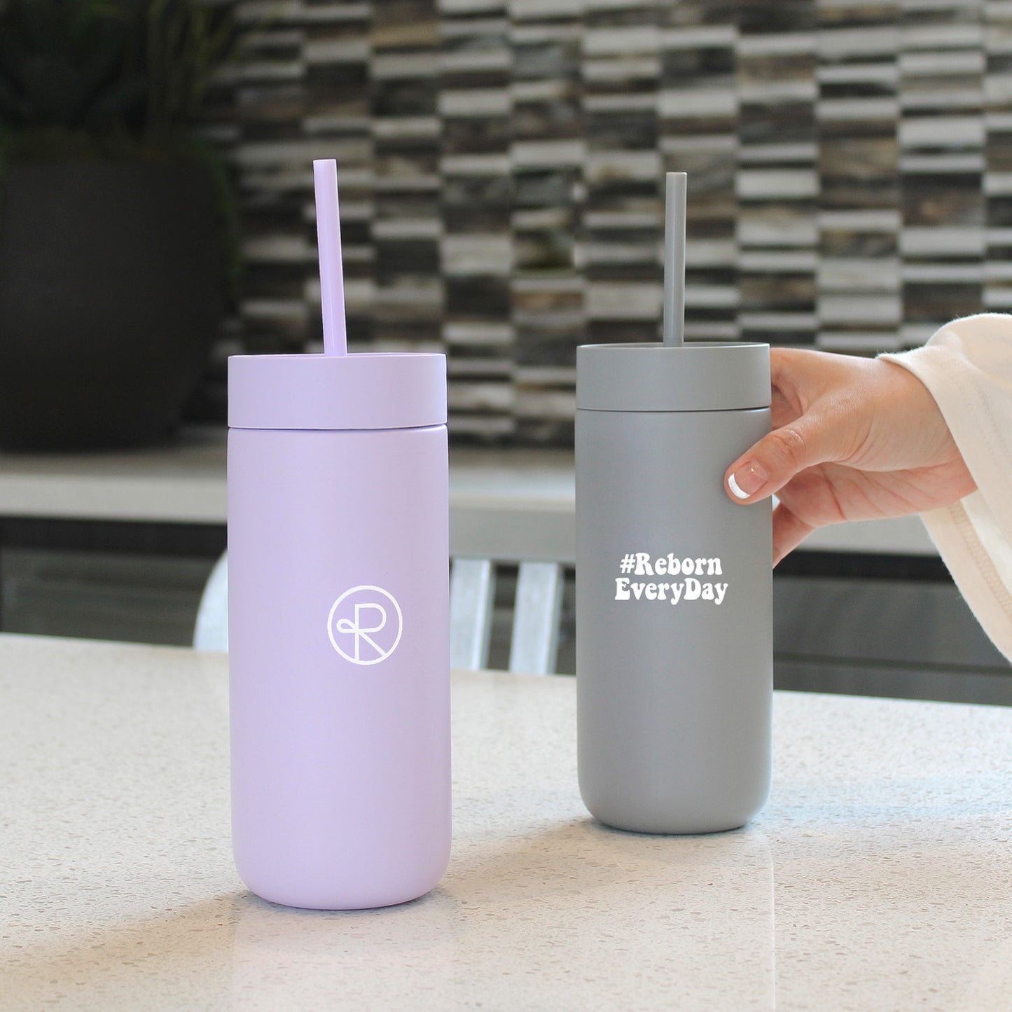 Grey and Lavender Fellow Tumblers with Straws. Lavender tumbler has reborn logo on front, grey tumbler has #RebornEveryDay on front.
