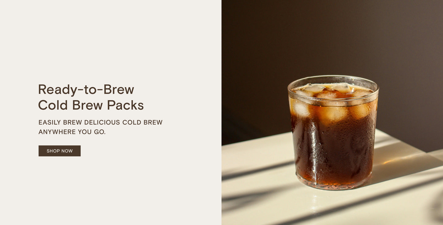 Glass of iced cold brew coffee on a sunlit surface next to text promoting ready-to-brew cold brew packs.